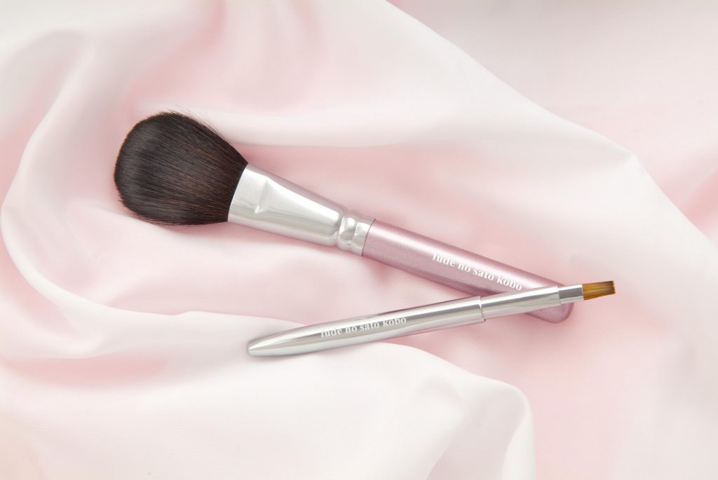 柔らかいピンクの布の上に2本熊野筆の化粧筆が並んでいる
