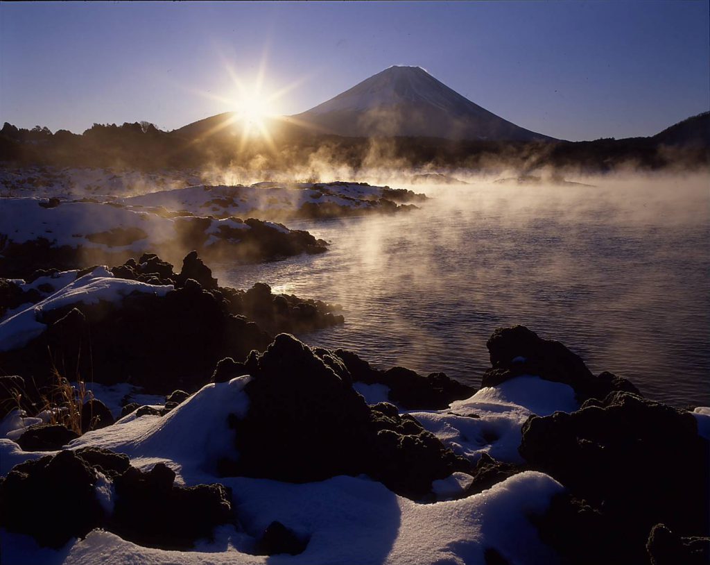 山梨県富士河口湖町の本栖湖から見た富士山。雪景色の中朝日を背に浴びる富士山のシルエットが堂々としている。