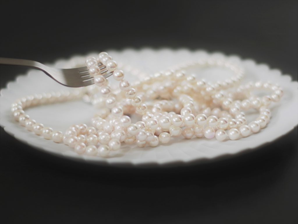 白いデザート皿に真珠のネックレスが載せてあって、フォークでそのネックレスを巻こうとしている