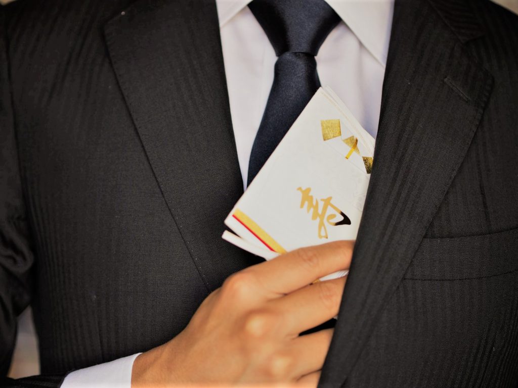 スーツの内ポケットから金色の文字で寿と書かれたご祝儀袋を出す様子。