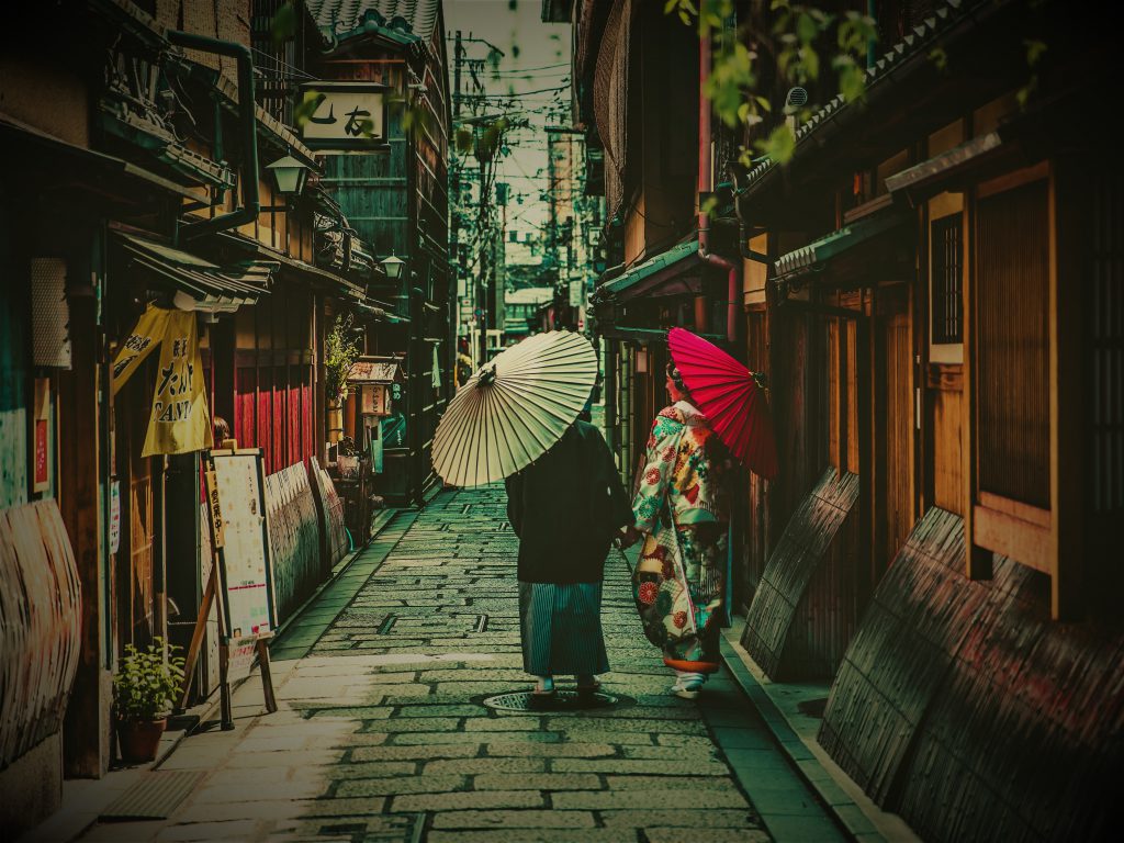 白い和傘を男性が、赤い和傘を女性がさして古き良き街並みを和服姿で歩いている様子。