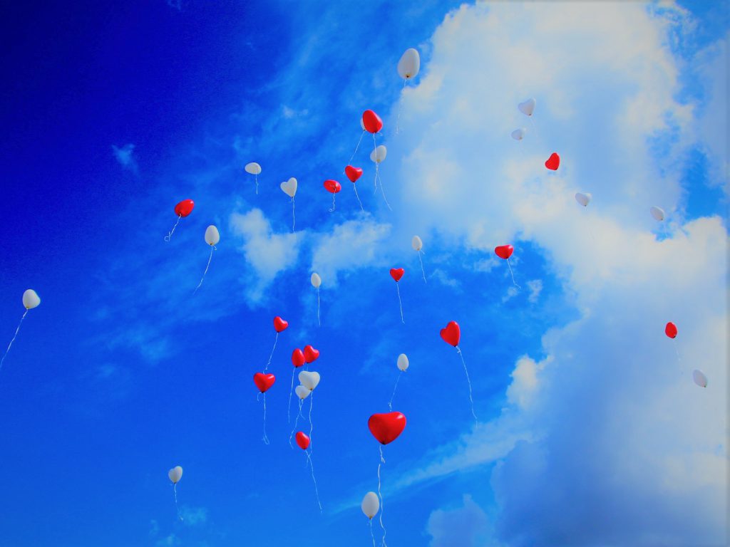 青空に白い雲、赤と白のハートの風船が無数に空に向かって飛んでいく様子
