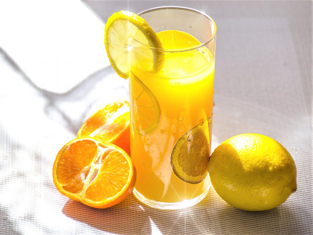 日差しの入るテーブルの上にグラス一杯のオレンジジュースとレモンとオレンジが置いてある