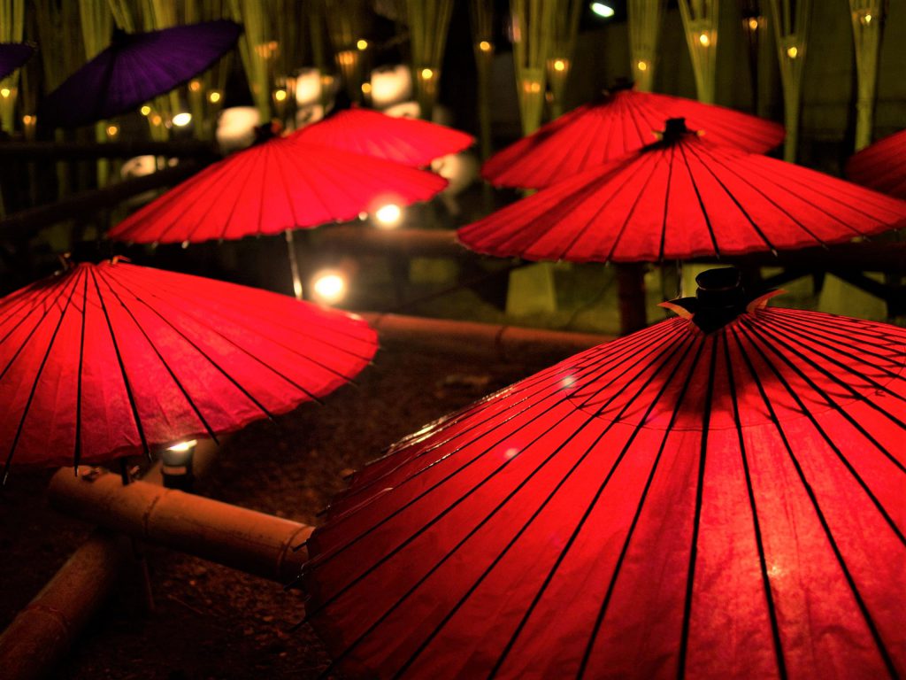 赤い和傘がたくさん並び金色の光でライトアップされている幻想的な写真。