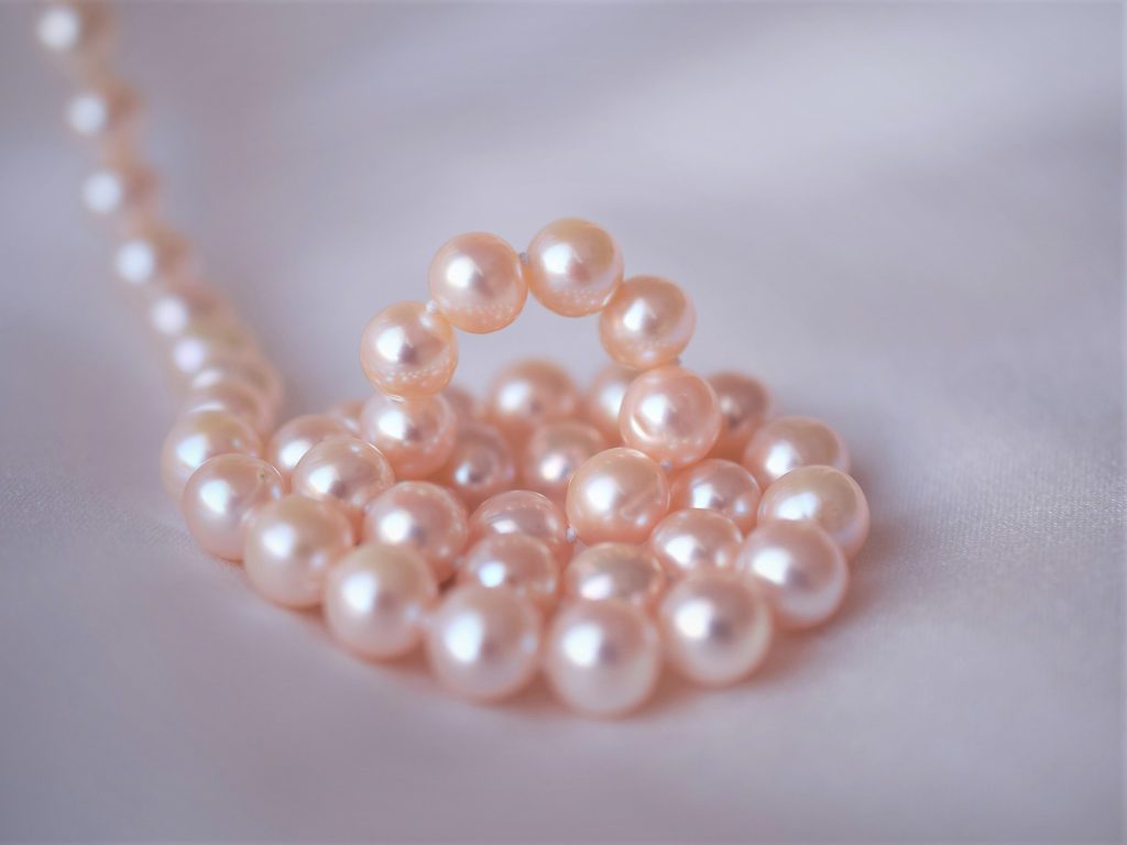 白いシーツの上にピンク色の輝く真珠が巻かれている