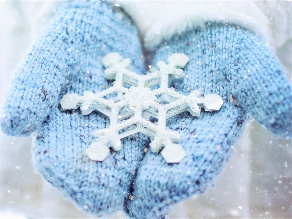 青いミトンのかわいらし手袋の両手に雪の結晶が入っていて、差し出している写真。