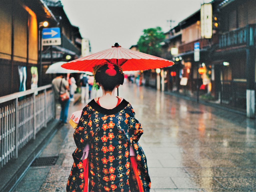 古い街並みを舞妓さんが赤い和傘をさして歩く後ろ姿。