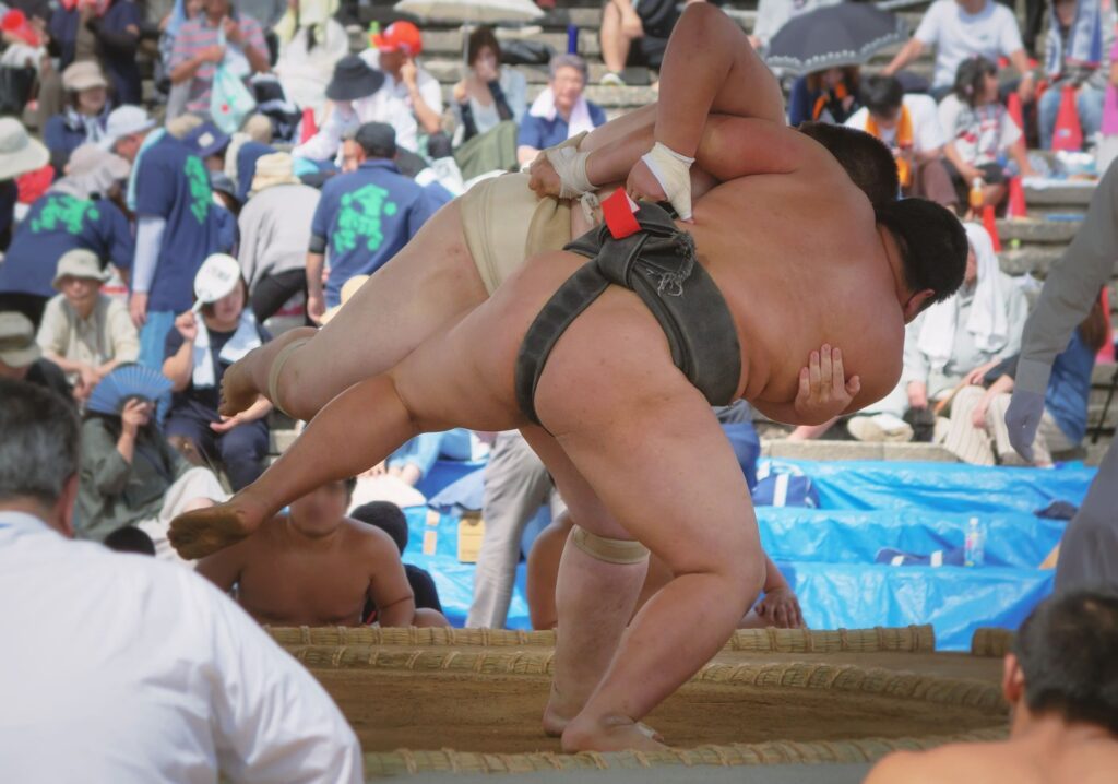 Two sumo wrestlers grappling in an outdoor sumo ring during a match