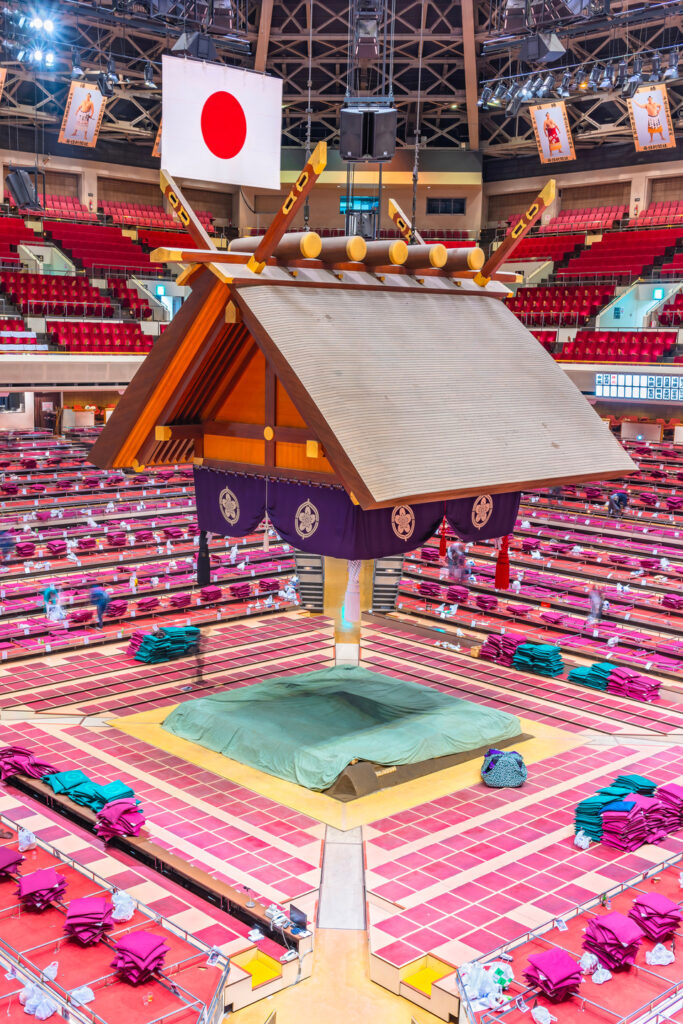 Interior view of a Grand Sumo arena with the dohyo and suspended roof before a tournament