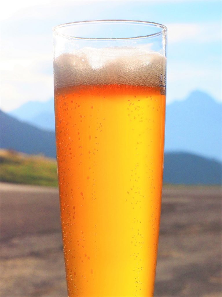広大な大地と青空の下、山々が後ろに取り囲む中に黄金色に輝くキンキンに冷えたグラスビール