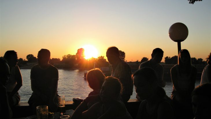 夕日を見つめながらお酒を片手に楽しく語らう人々