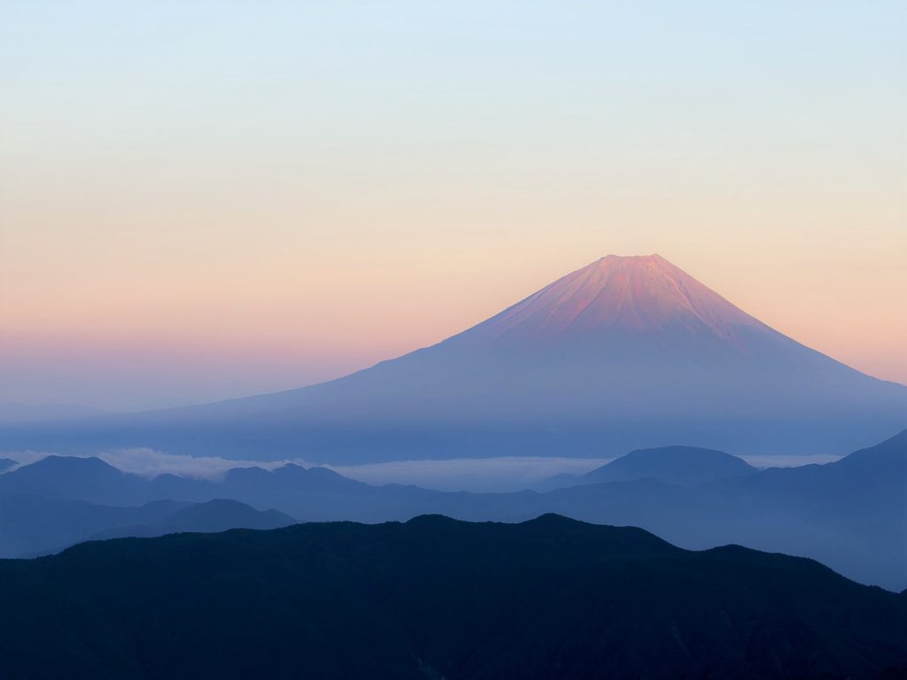 朝焼けもしくは夕日のうっすらブルーからオレンジ色に変わる空と美しい富士山の写真