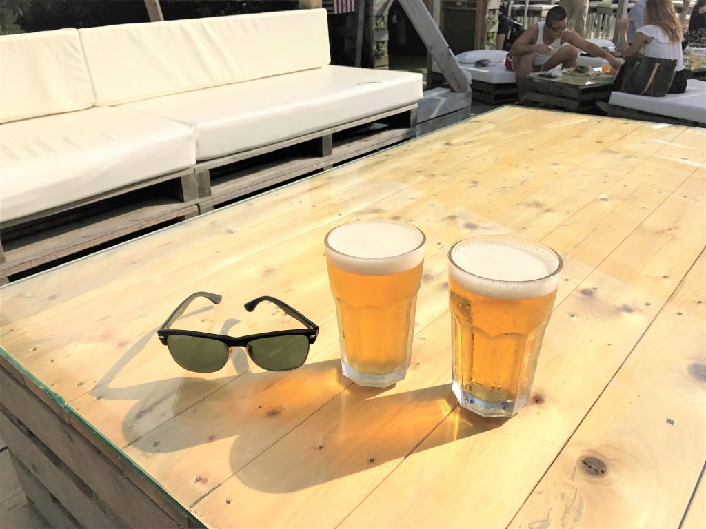 逗子葉山にあるカフェのテーブルにサングラスとビールが2杯置いてある。奥には白いソファ。
