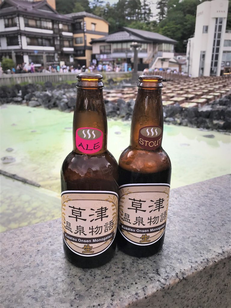 草津の湯畑をバックに草津のクラフトビール。エールとスタウトの2種類の瓶が並んでいる。