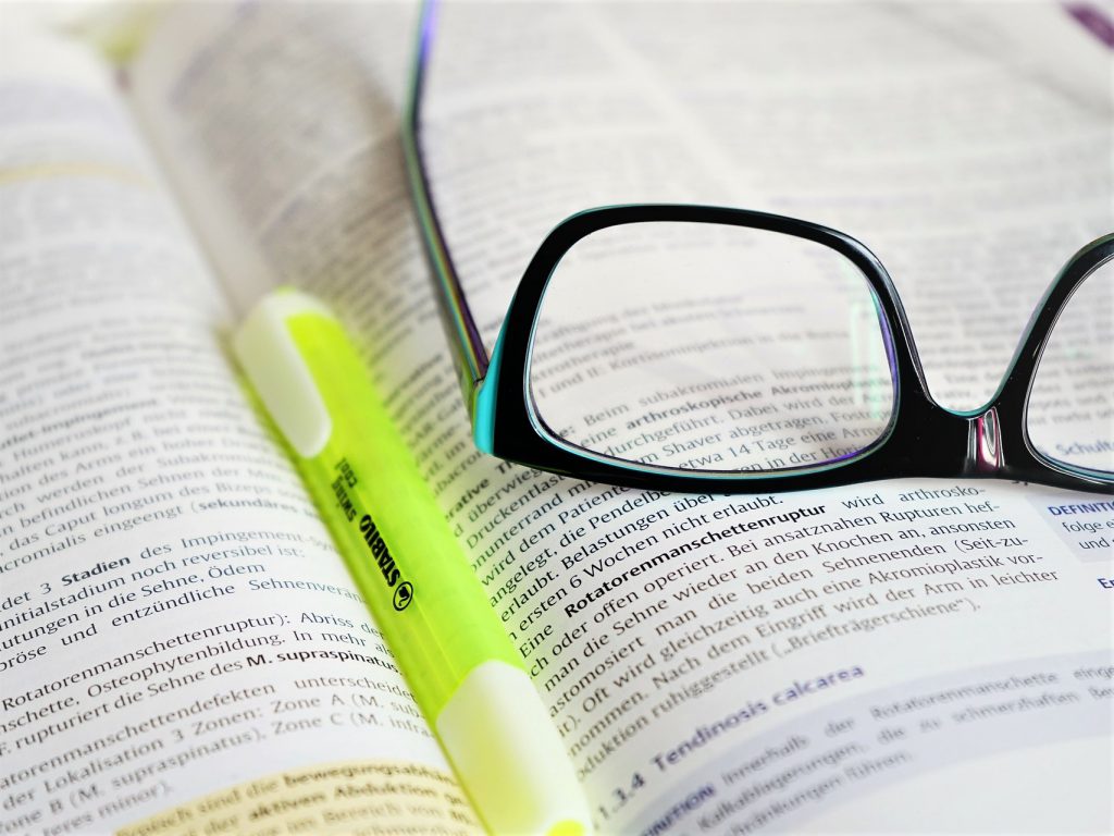 参考書か英字の本の上に黒ぶちの眼鏡と黄色い傾向マーカーが置いてある写真