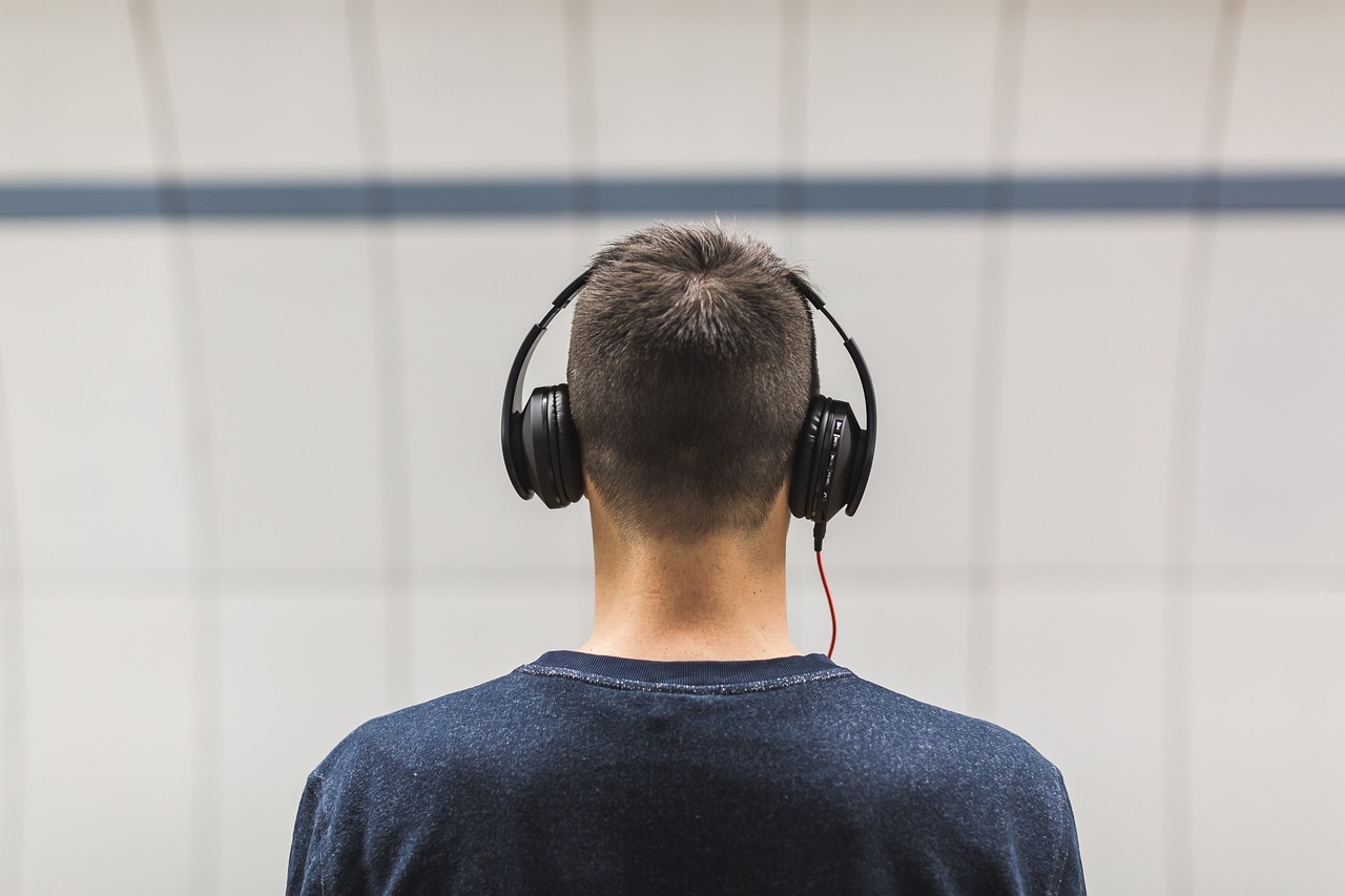 街中でヘッドフォンを身に着け、電車を待っている人の後ろ姿。