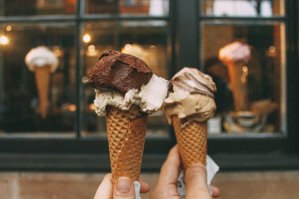 コーンに乗せられたチョコレートアイスクリーム2つを重ね合わせアイスクリーム屋さんのディスプレイの前で撮影している様子