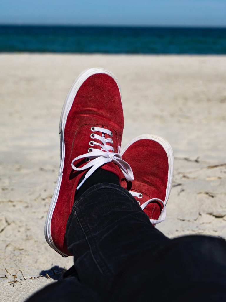 白い浜辺に海の見えるところで赤いスニーカー。