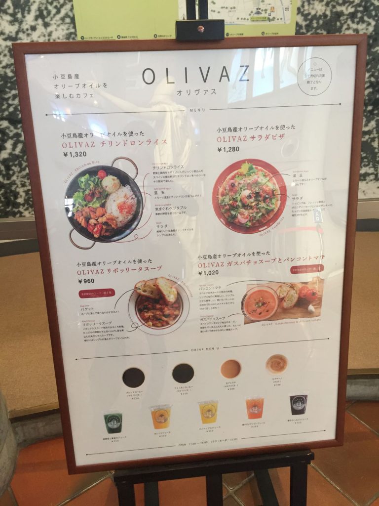 カフェ『オリヴァス』のメニュー板。「チリンドロンライス」や「サラダピザ」など、美味しそうな写真が並ぶ。