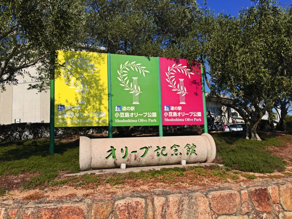 オリーブ公園内のオリーブ記念館案内看板の様子。文字がオリーブ色をしている。