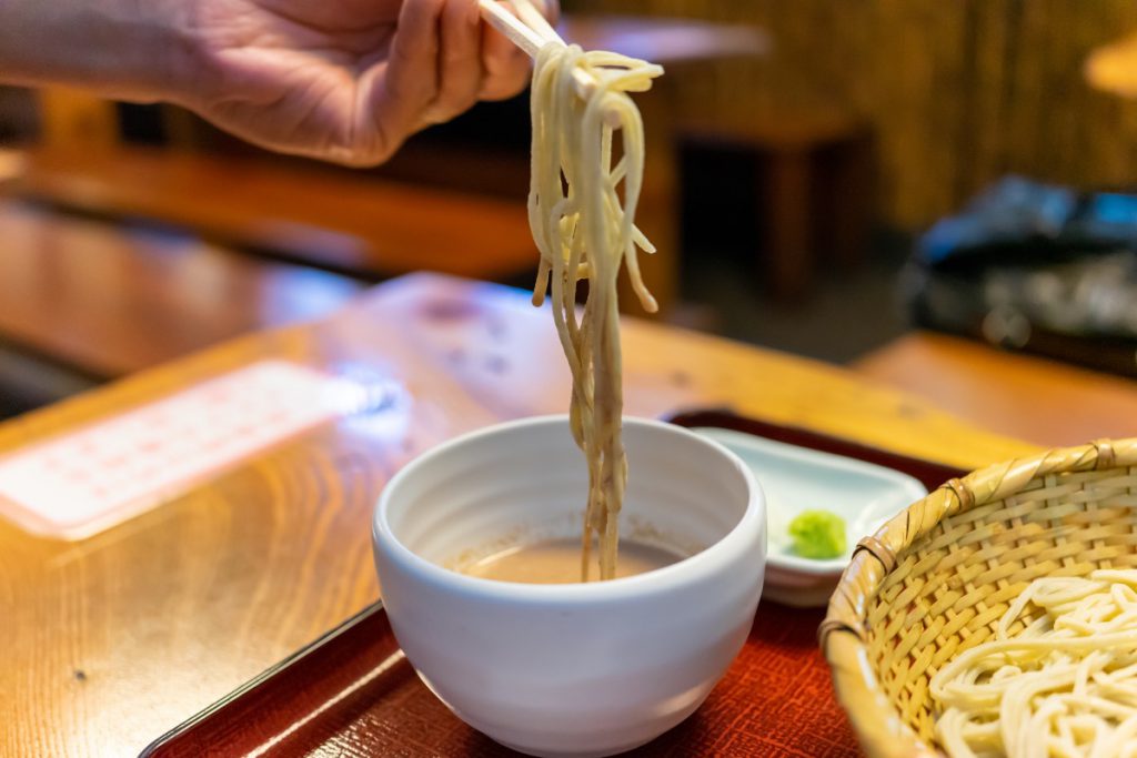 深大寺そば「一休庵」の「十割 胡桃だれそば」をタレにつけているところ