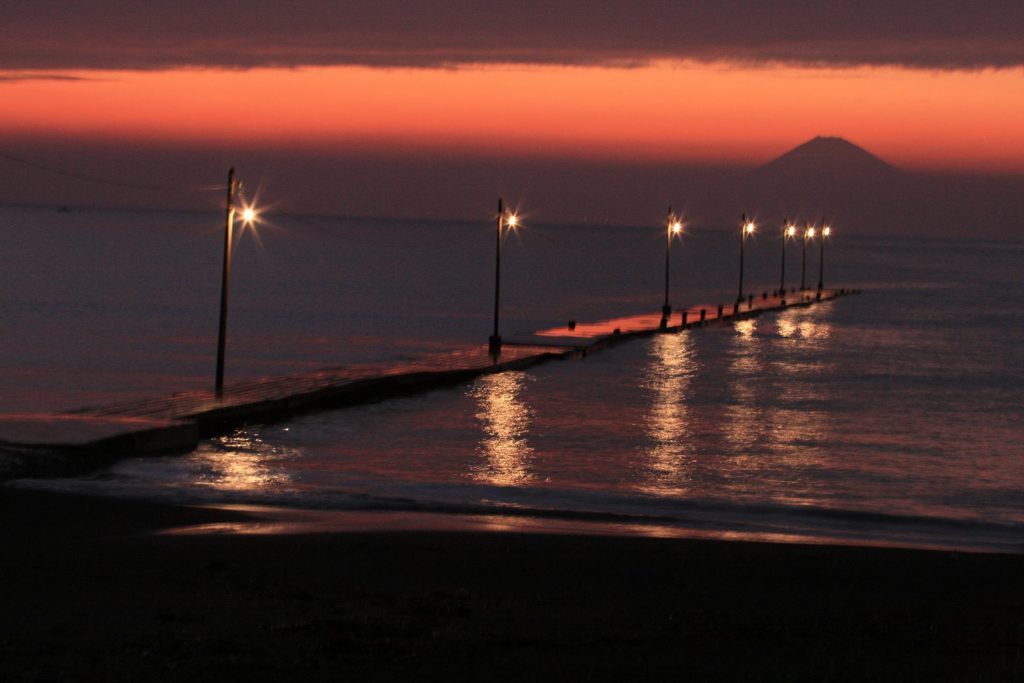 原岡桟橋夕方の様子。電柱に灯りが灯り、海の向こうにはうっすら富士山が見える。