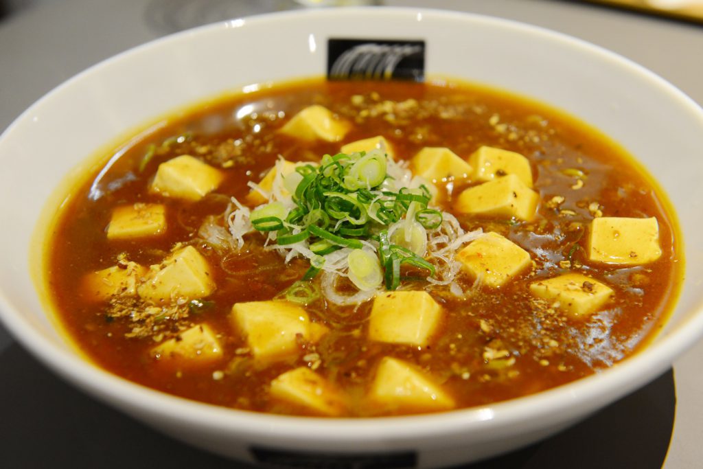 白い器に入った麻婆京豆腐うどん。小口に切ったネギが中央にのせられています。