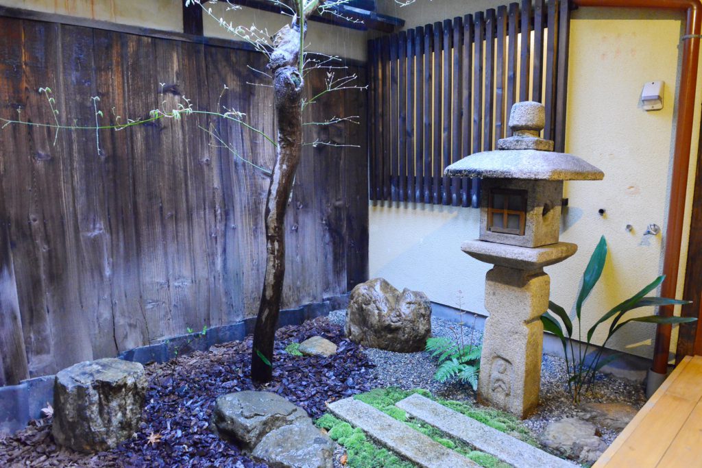 京都の風情を感じる、お店の庭の風景。右側に灯ろう、真ん中に木があります。
