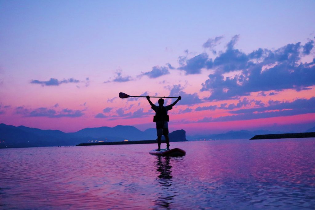 東かがわの山田海岸で美しい夕日を見ながらSUP「Stand Up Paddleboard（スタンドアップパドルボード）」を楽しむ様子。