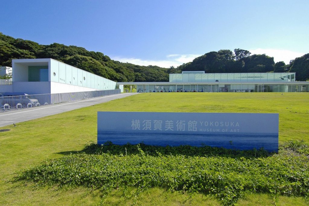 The strikingly modern and beautiful exterior of the Yokosuka Museum of Art, set against a blue sky and green lawns.