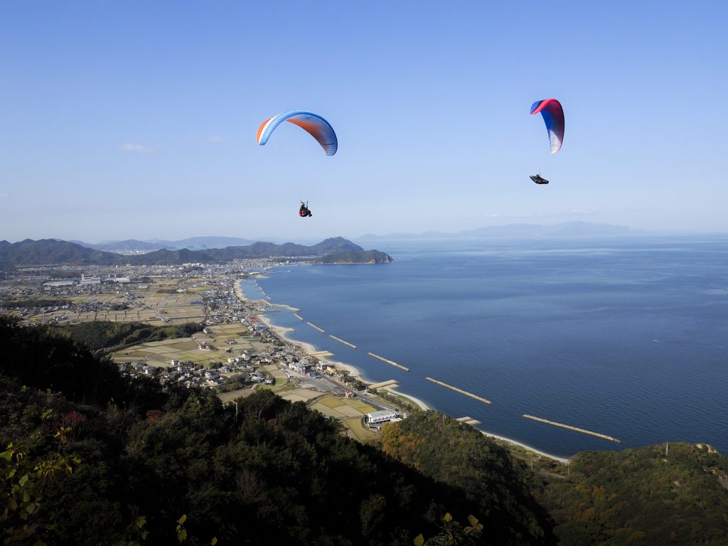 快晴の下「大坂峠」でパラグライダーを楽しんでいる様子。