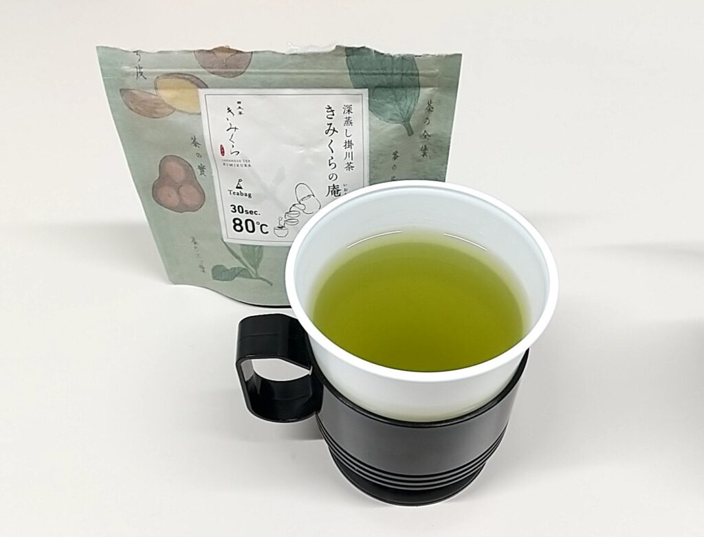 「日本茶きみくら」の商品「Art Print Package (Teabag) Collection」の1つ、羽田店限定の「深蒸し掛川茶 きみくらの庵」。緑系のパッケージの手前にはお茶が入ったコップが置かれている。