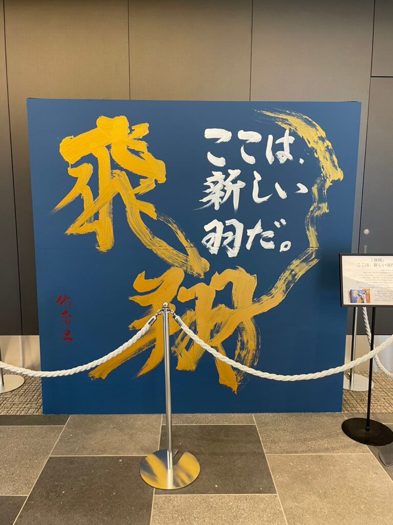 「羽田エアポートガーデン」開業セレモニーで、書道家によって披露された書道パフォーマンスの作品。青い用紙に金文字で「飛翔」と書かれている。