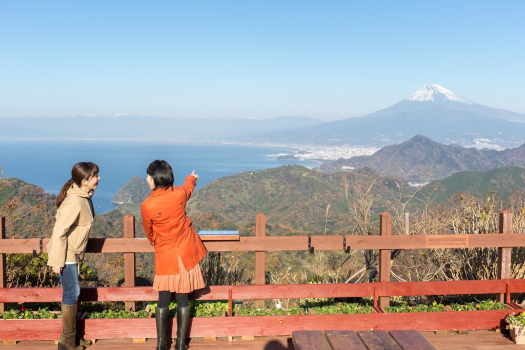 静岡県伊豆の国市の「伊豆パノラマパーク」の展望デッキからの眺め。女性二人組が富士山を指差しながら景観を見ている。