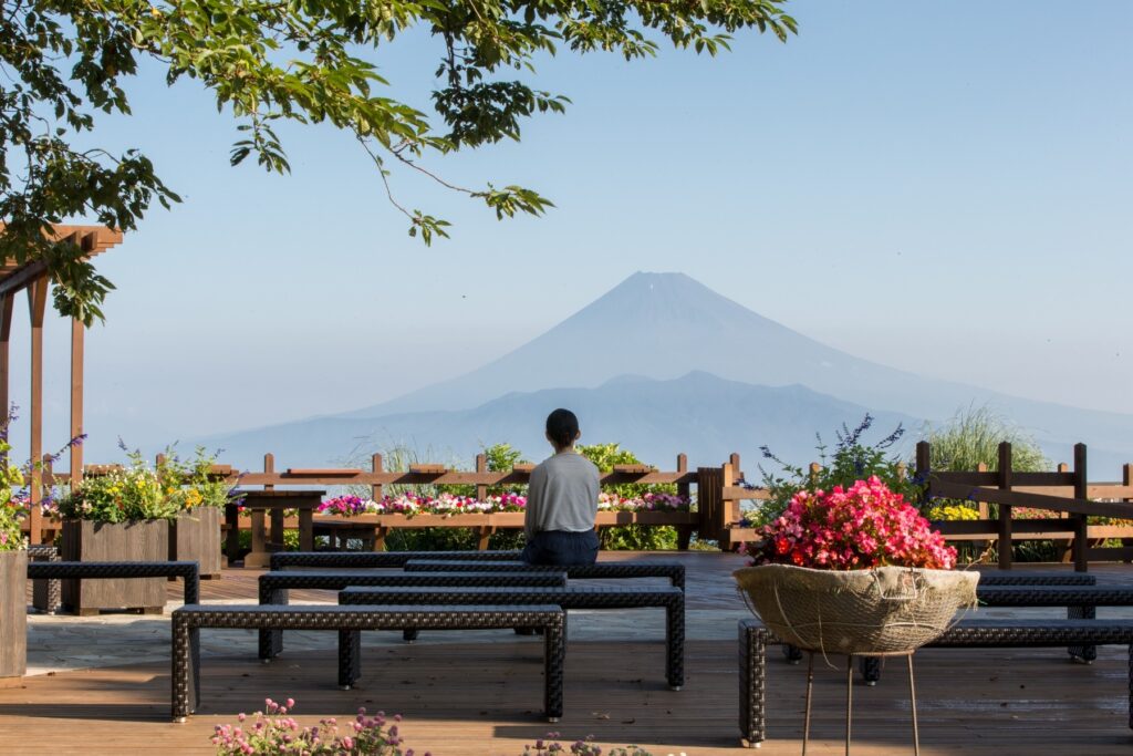 静岡県伊豆の国市「伊豆パノラマパーク」の展望テラス。ベンチに座って女性が1人富士山を眺めている。