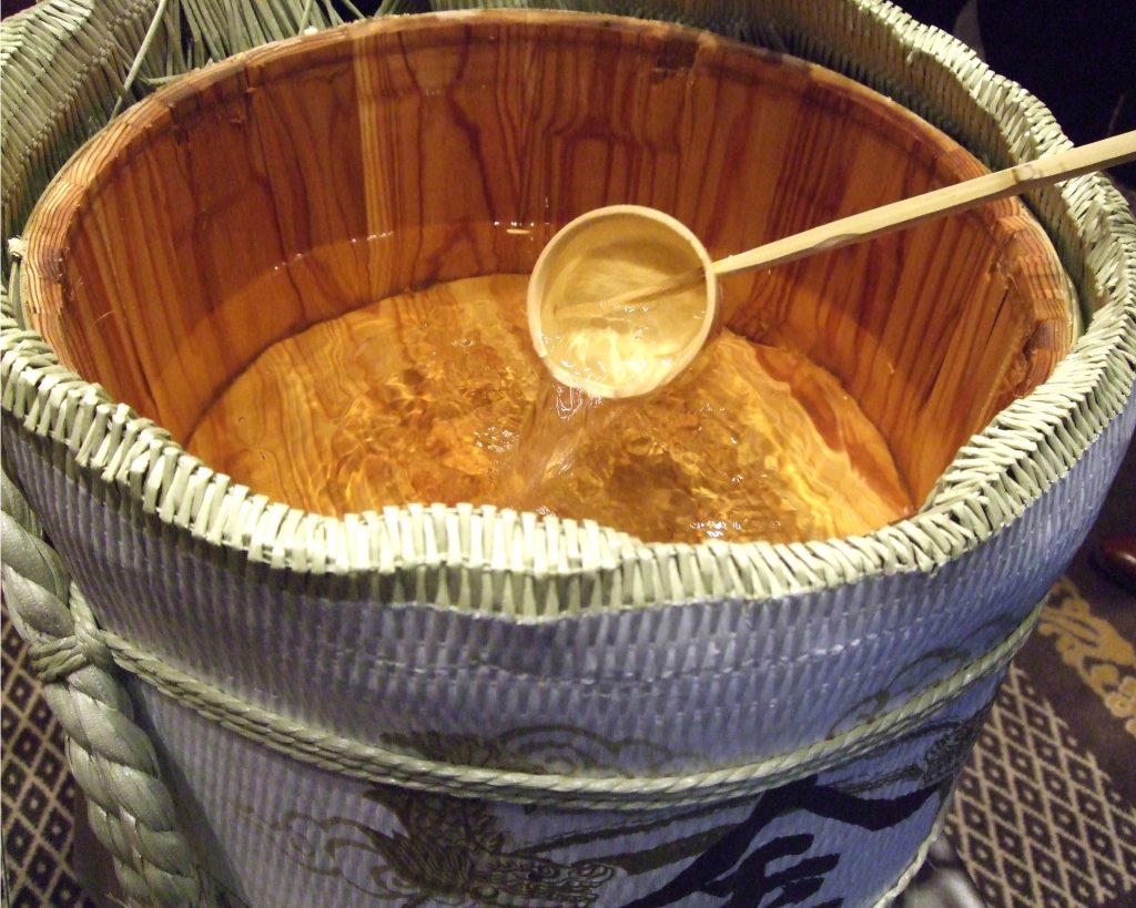 木樽に大量に入った日本酒を柄杓ですくっている