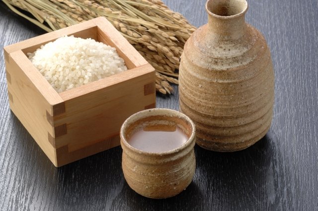 茶色の陶器のトックリとおちょこ。日本酒の原料米のお米が枡に入っている。