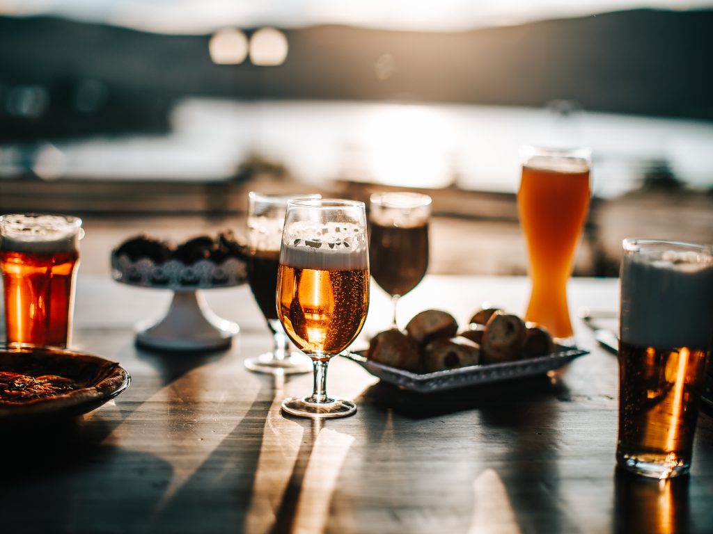 海が見えるテラス席にオリーブなどのおつまみとグラスに注がれたビールが太陽の光を浴びて輝いている様子