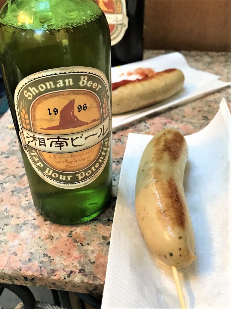 湘南ビールの緑の瓶と、櫛に刺さったソーセージが並んでいる写真