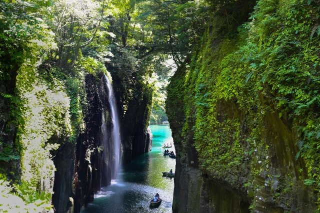 高千穂峡の峡谷から滝のような水が流れでている。その横を貸しボートで進む観光客の様子。