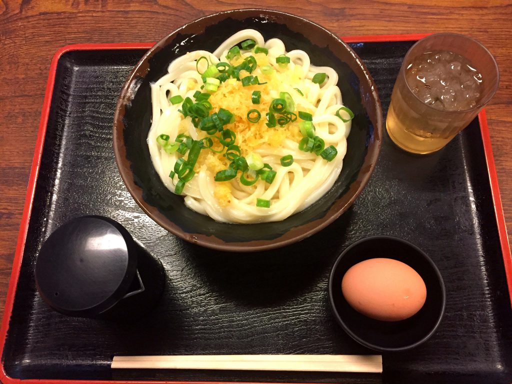 おぼんに乗っている「うどんバカ一代」の窯玉うどん。卵、お醤油、お箸、お水がお盆に乗っている。