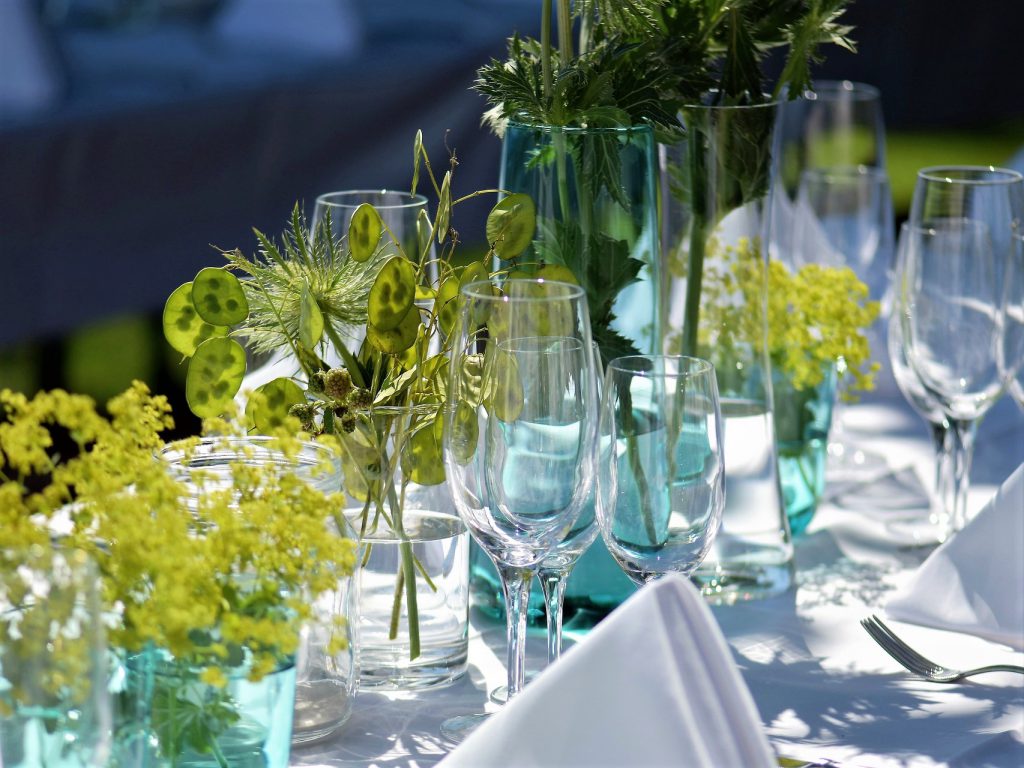 テーブルの上に青や透明のワイングラスと装飾の緑が飾られたガーデンパーティーの様子