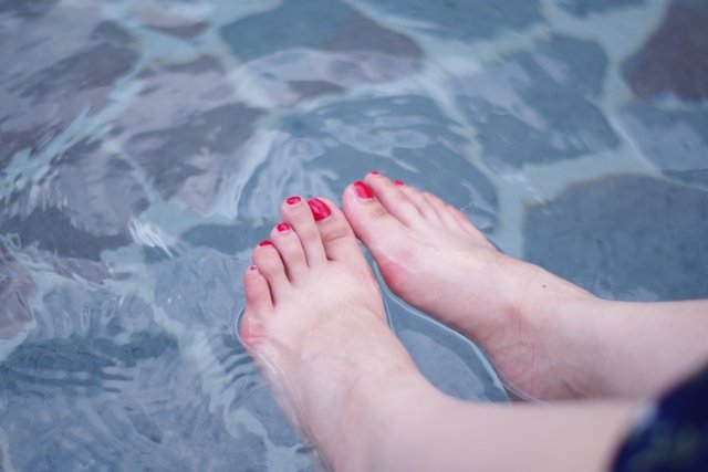 足湯に浸かっている赤いペディキュアを塗った足。