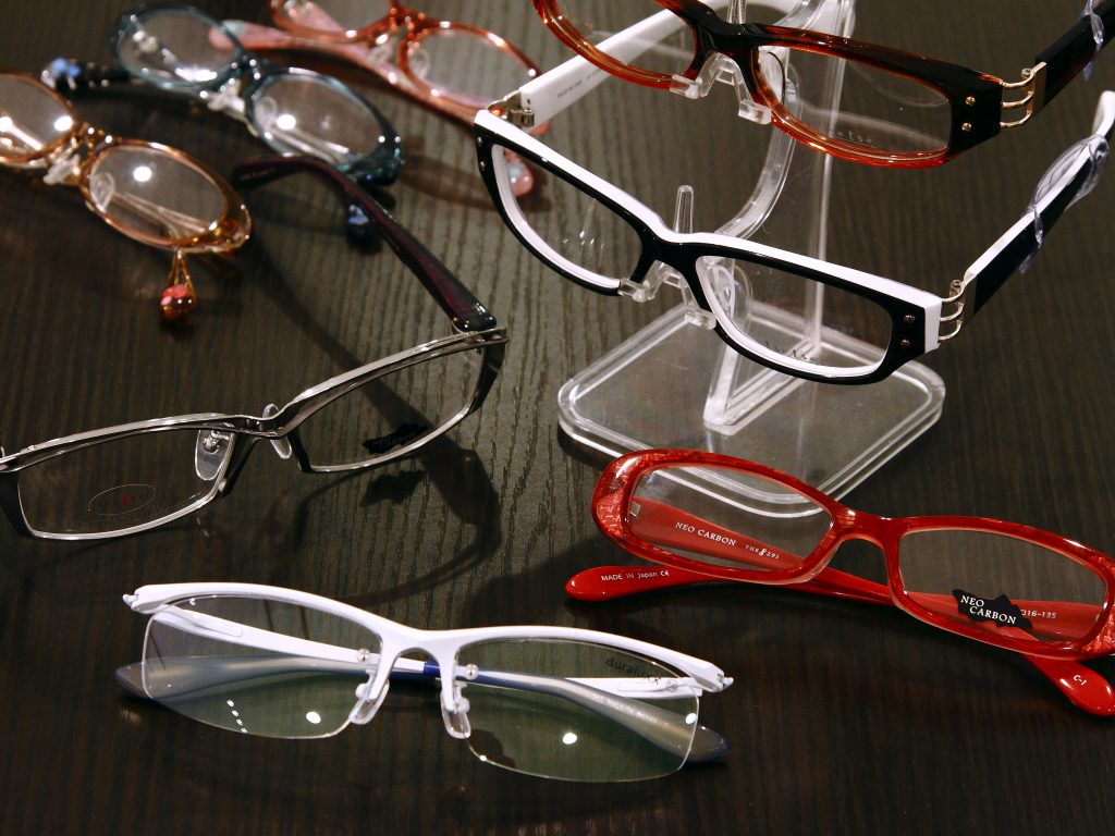 黒いテーブルの上に赤や白や黒のプラスチックまたはセラミック素材の眼鏡がたくさん置いてある写真。