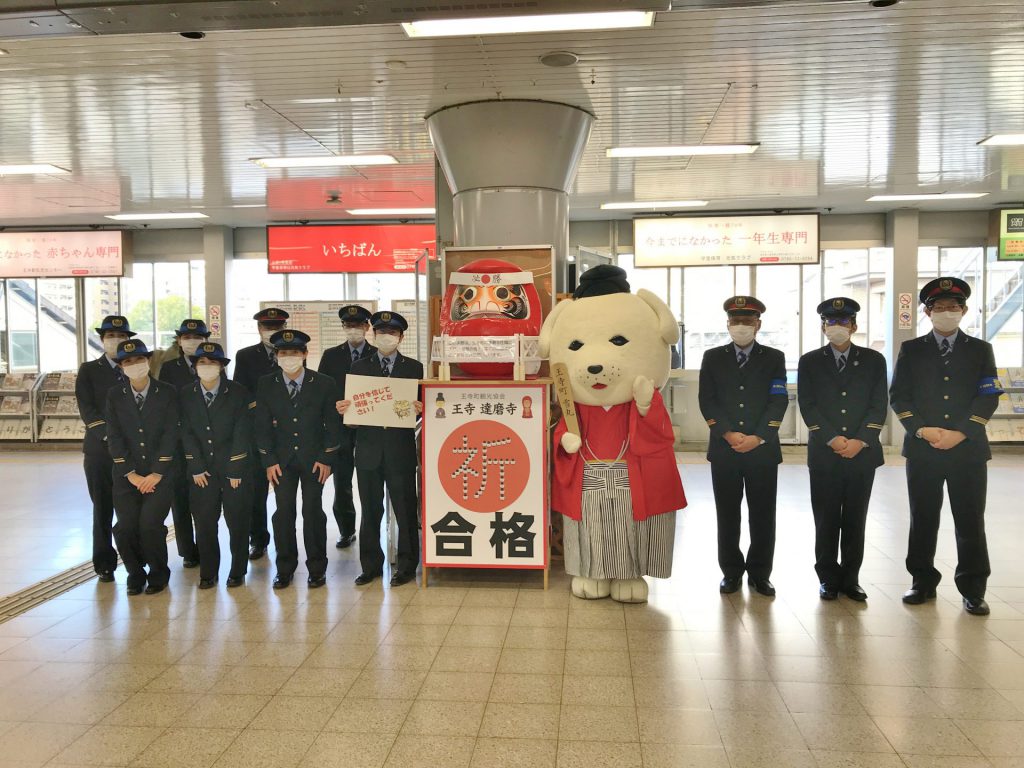 駅員さんが数名並んでいて、真ん中に雪丸がいる。合格だるま展示ストリートをしている様子。