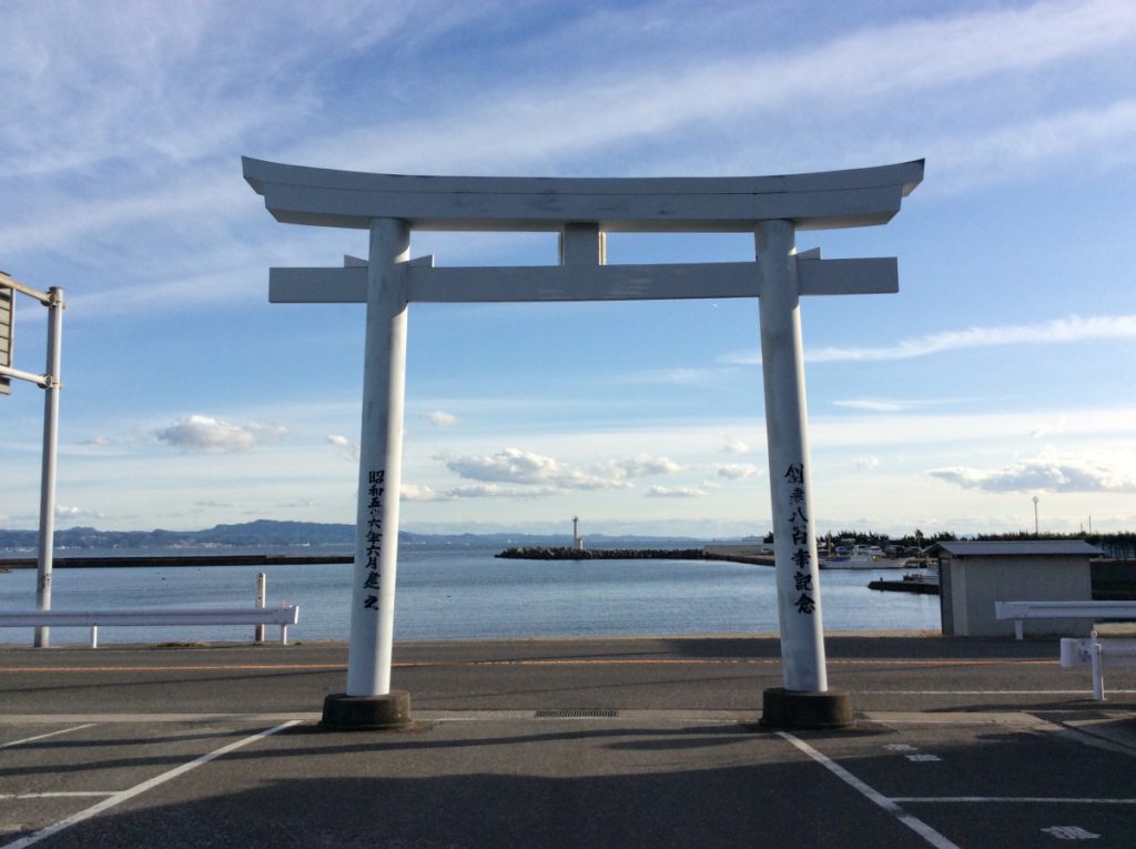 横須賀の「鴨鶴」の駐車場にある目印の白い鳥居とその向こうにある海が青空のもと美しい