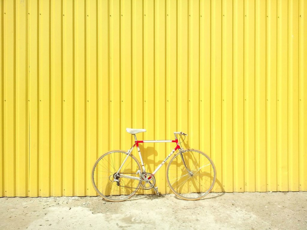 黄色のトタン壁の前に白い自転車が置かれている。