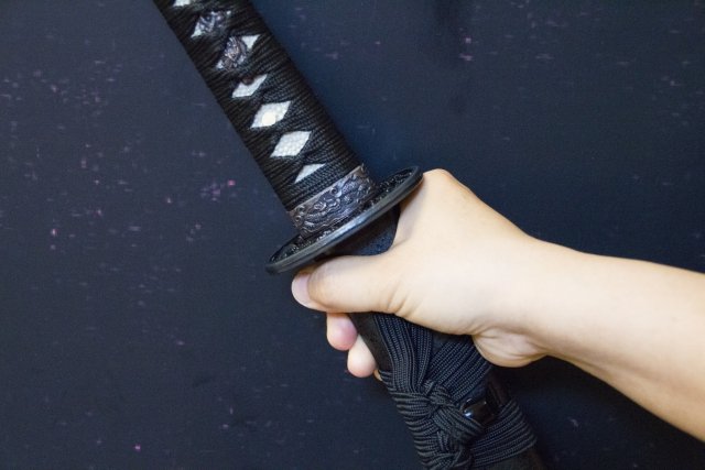 黒い装飾の日本刀を手に握っている様子。