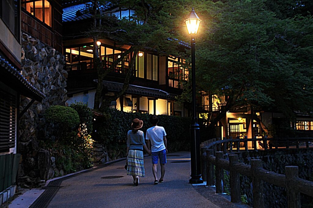 ライトアップされている夜の橋と明治建築の建物のある通り。男女のカップルが手を繋いで渡っている。