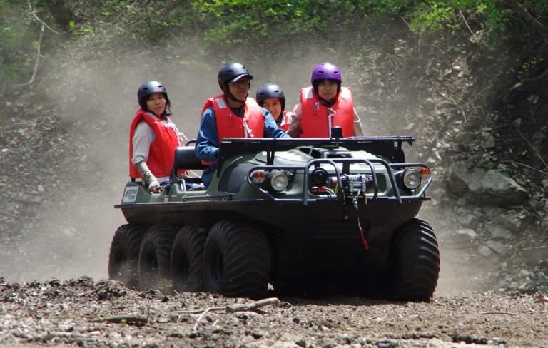 タイヤが８個付いた水陸両用車に人が4人乗っている様子。